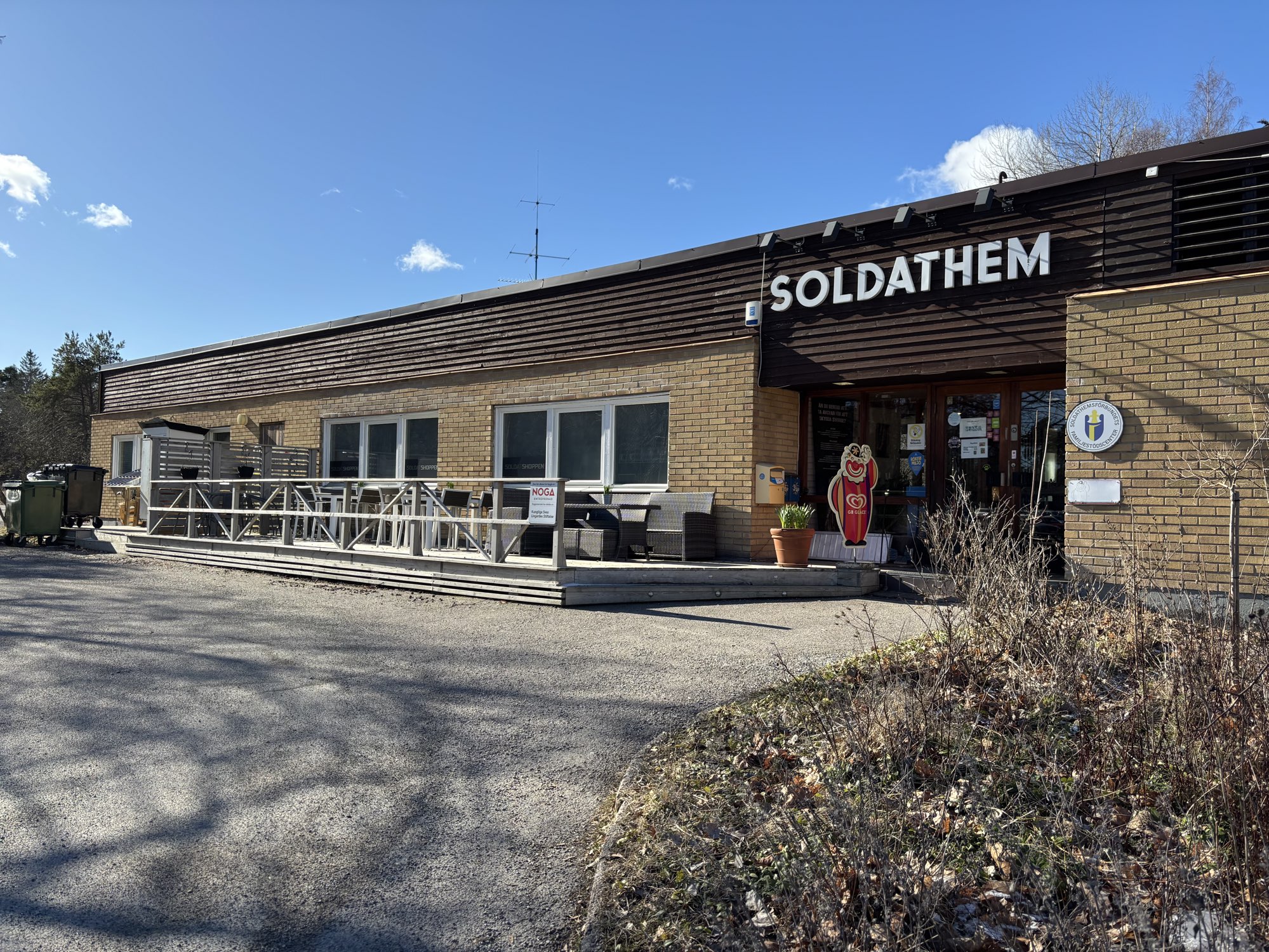 Fasaden på Soldathemmet utanför Livgardet. En låg brun byggnad med en veranda med utemöbler utanför. Och en GB-glassgubbe!