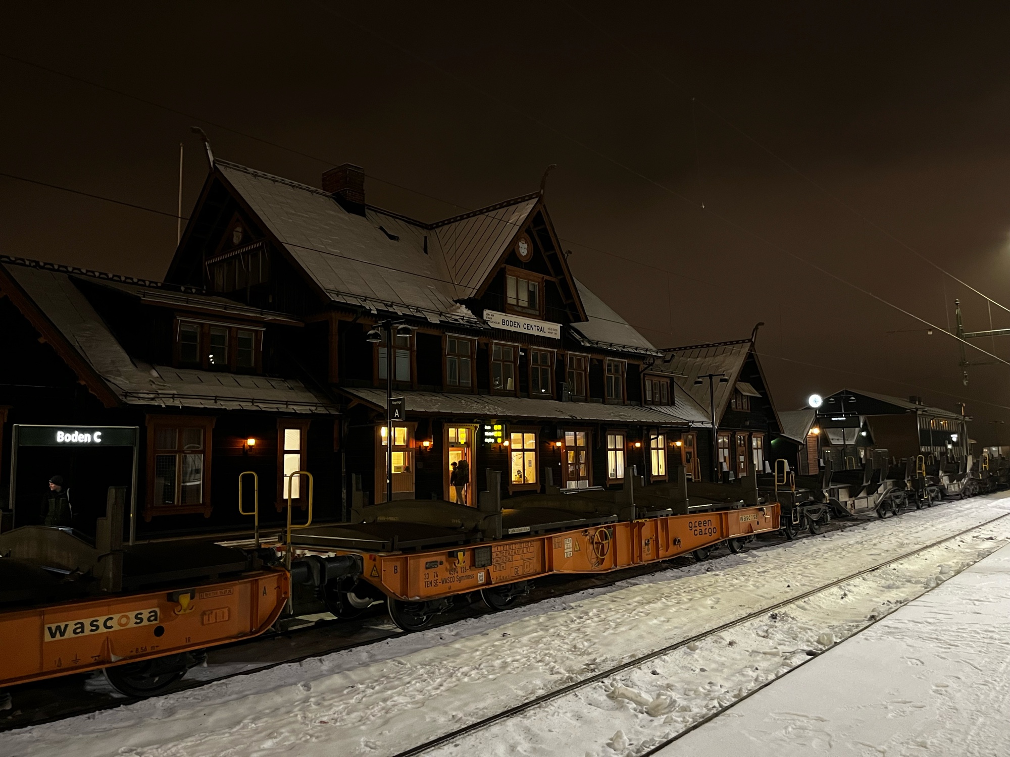 Bodens tågstation, i mörker med upplysta fönster och lite snö. Framför står en lång rad godsvagnar, men utan gods på. 